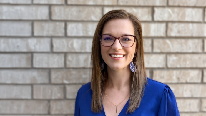 East Texas A&M alum Tina Clark wearing a blue top, standing against a light brick background.